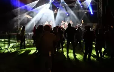 widzimy grupę os&oacute;b stojących pod sceną, na kt&oacute;rej występuje zesp&oacute;ł