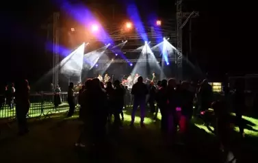 widzimy grupę os&oacute;b stojących pod sceną, na kt&oacute;rej występuje zesp&oacute;ł