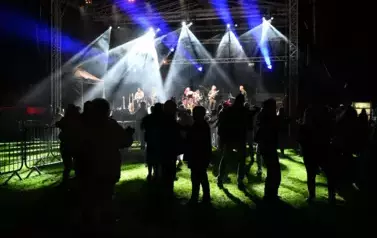 widzimy grupę os&oacute;b stojących pod sceną, na kt&oacute;rej występuje zesp&oacute;ł