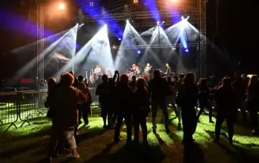 widzimy grupę os&oacute;b stojących pod sceną, na kt&oacute;rej występuje zesp&oacute;ł
