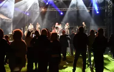 widzimy grupę os&oacute;b stojących pod sceną, na kt&oacute;rej występuje zesp&oacute;ł