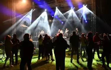 widzimy grupę os&oacute;b stojących pod sceną, na kt&oacute;rej występuje zesp&oacute;ł