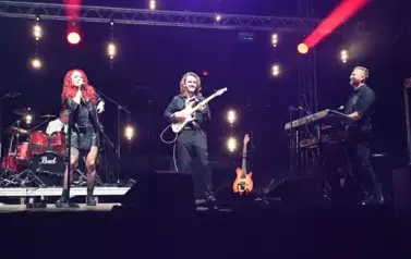 widzimy panią śpiewającą oraz dw&oacute;ch pan&oacute;w grających na instrumentach