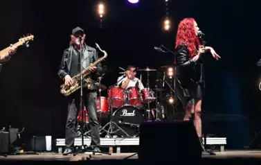 widzimy panią śpiewającą oraz dw&oacute;ch pan&oacute;w grających na instrumentach