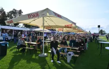 widzimy siedzące osoby na ławkach i pod parasolami