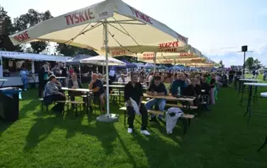 widzimy siedzące osoby na ławkach i pod parasolami