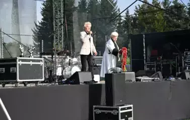widziy pana stojącego z mikrofonem w ręce oraz panią trzymającą kwiaty w rękach