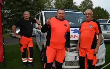 widzimy trzech ratownik&oacute;w medycznych oraz stojącą za nimi karetkę 