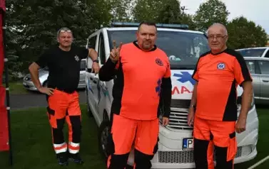 widzimy trzech ratownik&oacute;w medycznych oraz stojącą za nimi karetkę 