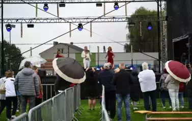 widzimy kilka os&oacute;b słuchającą koncertu oraz pana i dwie panie śpiewające do mikrofonu