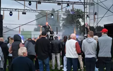 widzimy kilka os&oacute;b słuchającą koncertu oraz dw&oacute;ch pan&oacute;w śpiewających na scenie i pana stojącego z tyłu