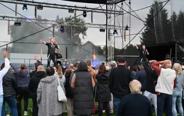 widzimy kilka os&oacute;b słuchającą koncertu oraz dw&oacute;ch pan&oacute;w śpiewających na scenie i pana stojącego z tyłu
