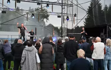 widzimy kilka os&oacute;b słuchającą koncertu oraz dw&oacute;ch pan&oacute;w śpiewających na scenie i pana stojącego z tyłu