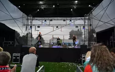 widzimy kilka os&oacute;b słuchającą koncertu oraz dw&oacute;ch pan&oacute;w śpiewających na scenie i pana stojącego z tyłu
