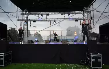 widzimy dw&oacute;ch pan&oacute;w śpiewających na scenie oraz pana stojącego w tle