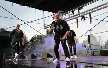 widzimy dw&oacute;ch pan&oacute;w śpiewających na scenie oraz pana stojącego obok z telefonem w ręce 