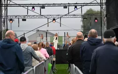 widzimy dużą grupę os&oacute;b słuchającą koncertu oraz osoby na scenie