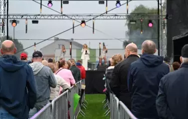 widzimy dużą grupę os&oacute;b słuchającą koncertu oraz osoby na scenie