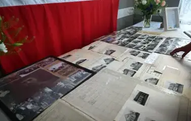 widzimy leżące na stole stare fotografie budynk&oacute;w oraz os&oacute;b