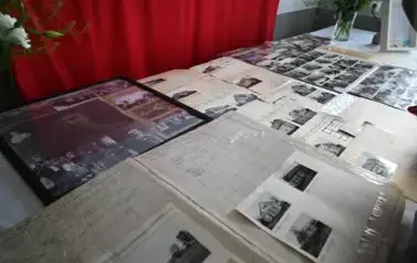 widzimy leżące na stole stare fotografie budynk&oacute;w oraz os&oacute;b