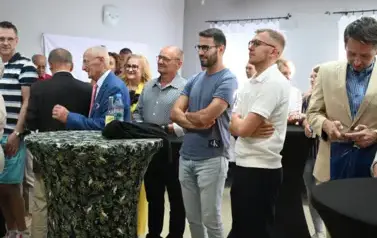 widzimy grupę os&oacute;b stojących obok stolik&oacute;w