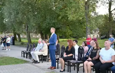 widzimy siedzące osoby na krzesłach oraz jednego pana stojącego 