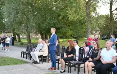 widzimy siedzące osoby na krzesłach oraz jednego pana stojącego 