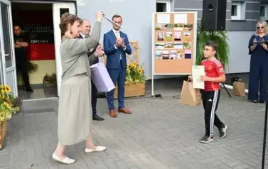 widzimy 2 pan&oacute;w oraz panią trzymającą upominek w ręce oraz chłopca idącego w jej kierunek