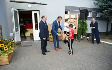 widzimy dw&oacute;ch pan&oacute;w przekazujących upominek chłopcu