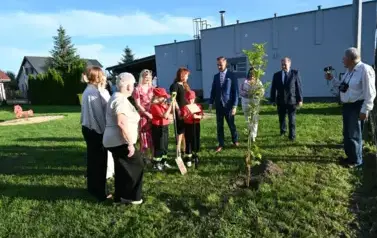 widzimy kilka os&oacute;b stojących oraz jedną osobę trzymającą łopate