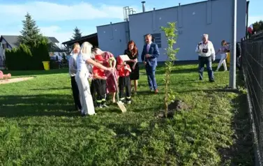 widzimy kilka os&oacute;b stojących oraz jedną osobę trzymającą łopate