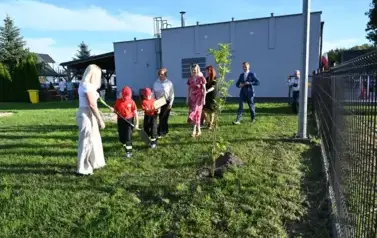 widzimy kilka os&oacute;b stojących oraz jedną osobę trzymającą łopate