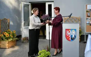 widzimy panią podającą kwiatka doniczkowego drugiej pani