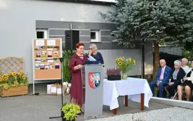 widzimy panią m&oacute;wiącą do mikrofonu oraz drugą panią stojącą w tle