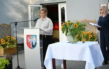 widzimy panią m&oacute;wiącą do mikrofonu oraz drugą panią stojącą w tle