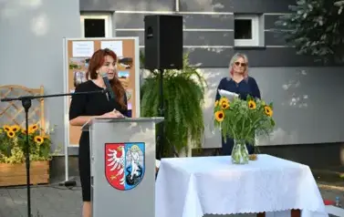 widzimy panią m&oacute;wiącą do mikrofonu oraz panią stojącą w tle