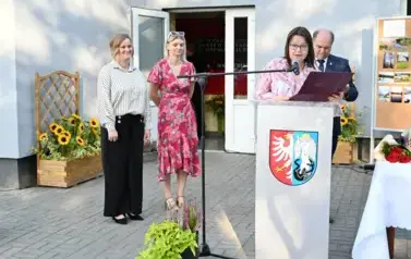 widzimy panią m&oacute;wiącą do mikrofonu oraz 2 panie oraz pana stojących za nią