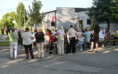 widzimy liczną grupę os&oacute;b stojąca bądź siedzącą na ławkach 