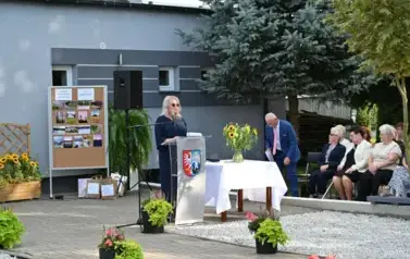 widzimy panią m&oacute;wiącą do mikrofonu oraz osoby siedzące na krzesłach