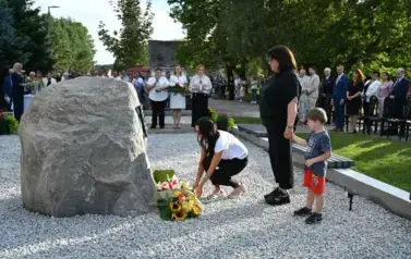 widzimy panią kładącą kwiaty przed pomnikiem oraz panią z chłopcem stojących na baczność