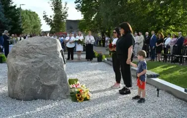 widzimy panią trzymającą kwiaty w rękach, drugą panią stojącą obok oraz chłopca