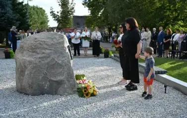 widzimy panią trzymającą kwiaty w rękach, drugą panią stojącą obok oraz chłopca