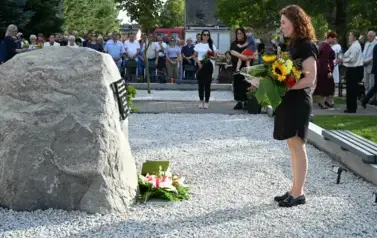 widzimy panią stojącą przed pomnikiem z kwiatami