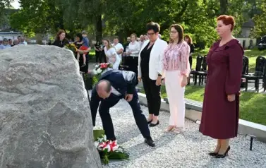 widzimy 3 panie stojące na baczność oraz pana kładącego kwiaty pod pomnikiem