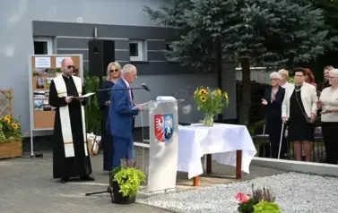 widzimy pana m&oacute;wiącego do mikrofonu oraz dwie osoby stojące za nim