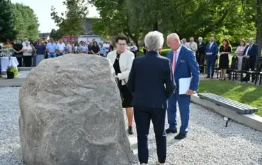 widzimy 3 osoby stojące przed pomnikiem oraz liczną grupę os&oacute;b w tle