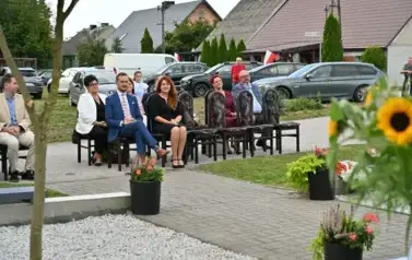 widzimy siedzące osoby na krzesłach oraz piękną nature oraz kwiaty wok&oacute;ł
