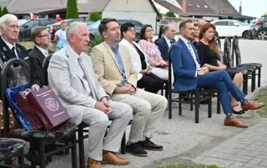 widzimy siedzące na krzesłach osoby oraz na jednym z krzeseł leżą dwie torby prezentowe