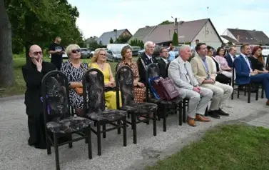 widzimy siedzące na krzesłach osoby oraz na jednym z krzeseł leżą dwie torby prezentowe