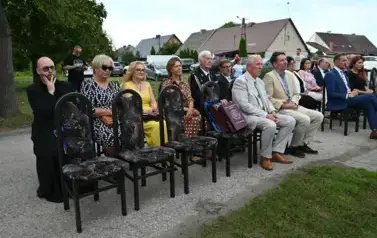 widzimy siedzące na krzesłach osoby oraz na jednym z krzeseł leżą dwie torby prezentowe